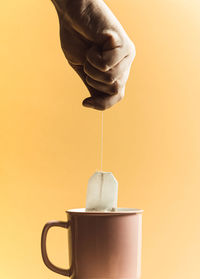 Cropped hand of person holding tea bag against colored background