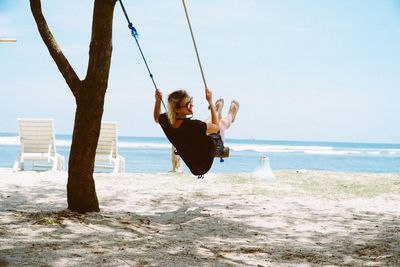 Rear view of woman on swing at beach