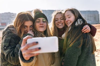 Four friends taking selfie with cell phone on the beach