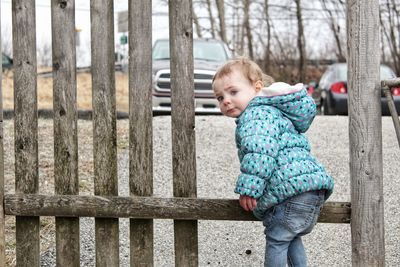 Full length of cute boy standing in fence against trees in winter