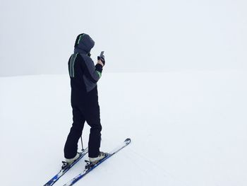 Side view of young woman using mobile phone while skiing on snow covered field