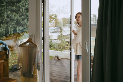 Smiling young woman opening door while entering in house