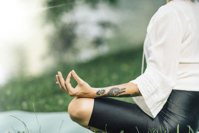 Young woman sitting in lotus position and practicing meditation near water in the nature