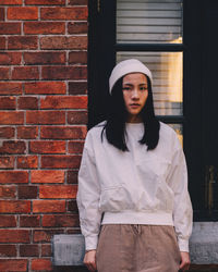 Portrait of young woman standing by brick wall