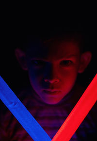 Close-up portrait of boy holding illuminated lighting equipment against black background