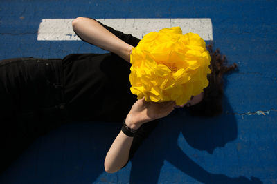 Young woman hiding face with yellow flower