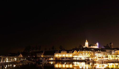 Illuminated buildings by river against sky at night