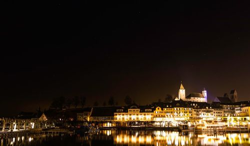 Illuminated buildings by river against sky at night