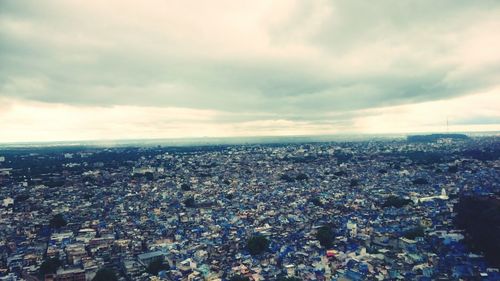 Aerial view of cityscape against cloudy sky