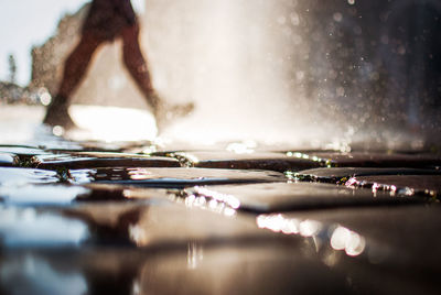 Low section of person walking on wet street by fountain