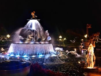 Illuminated fountain in city against sky at night