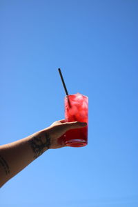 Close-up of hand holding red umbrella against blue sky