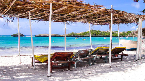 Empty deck chairs below thatched roof at beach