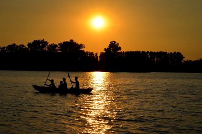 Silhouette people in sea against sky during sunset