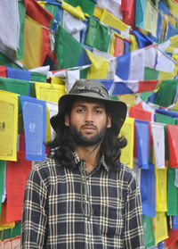 A bearded and long haired male tourist  looking at camera  standing against buddhist prayer flags 