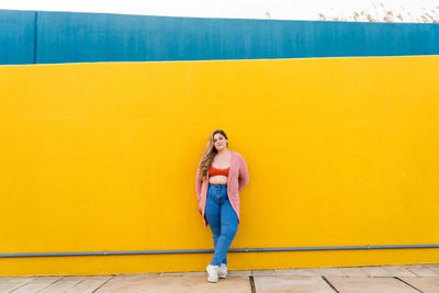 Full length of woman standing against yellow wall