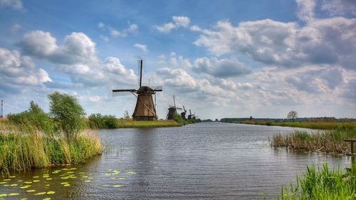 Traditional windmill on field by lake against sky