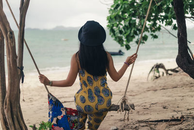 Rear view of woman sitting on swing at beach