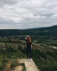 Rear view of woman standing on mountain against cloudy sky