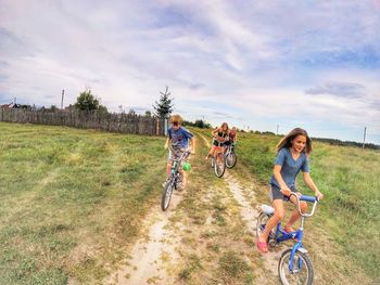 People riding bicycles on dirt road against sky