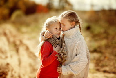 Two sisters in warm sweaters hug and run along the trail in the autumn forest. happy children