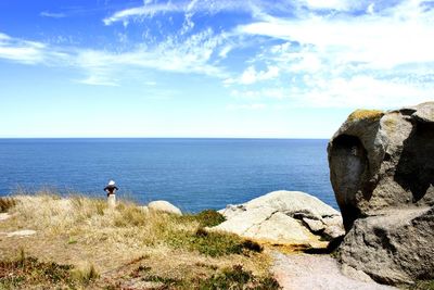 Man standing on rock by sea against sky