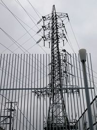 Low angle view of fence against electricity pylon