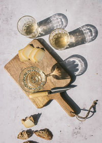 Top view composition with glasses of wine served with sliced cheese and bread with jam on marble table with wooden board in sunlight