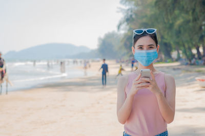 Portrait of woman using smart phone while standing at beach