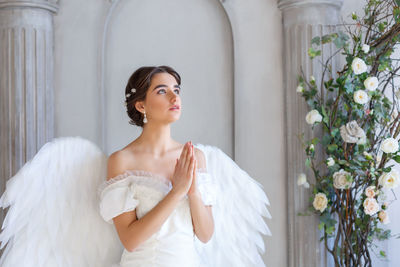 Portrait of a beautiful young woman in a white dress and angel wings, standing with a pleading 