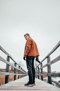 Low angle view of young man standing on footbridge against clear sky