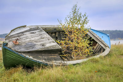 Abandoned boat moored on grass against sky