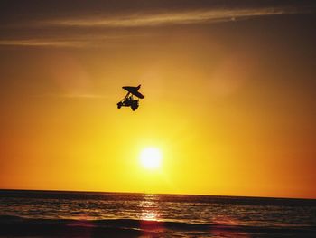 Silhouette helicopter flying over sea against sky during sunset
