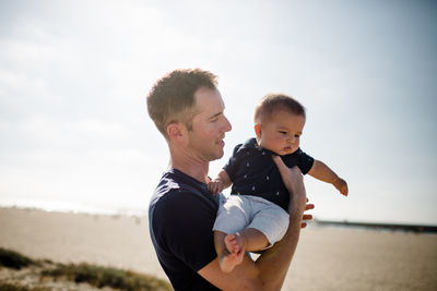 Father holding infant son on beach