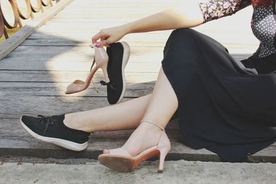 Low section of women holding shoes while sitting on footbridge