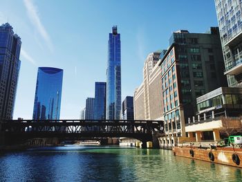 Modern buildings by river against sky in city