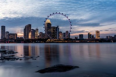 Illuminated city by river against sky