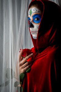 Woman with halloween make-up holding rose while standing amidst curtains