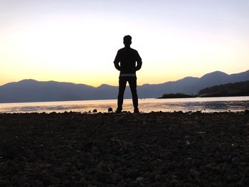 Rear view of silhouette man standing on beach against sky during sunset