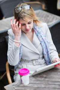 Young holding drink while using digital tablet on table