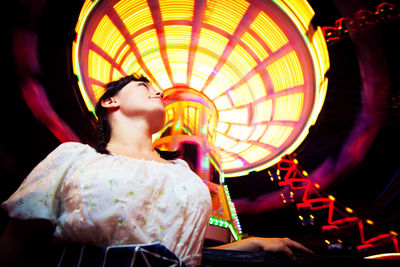 Low angle view of woman holding illuminated carousel at amusement park