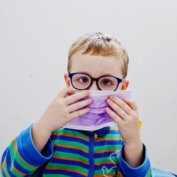 Portrait of boy with eyeglasses holding face mask against white background