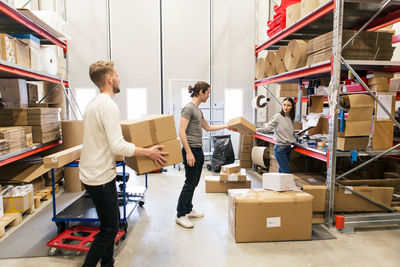 Full length of coworkers stacking boxes on rack standing at warehouse