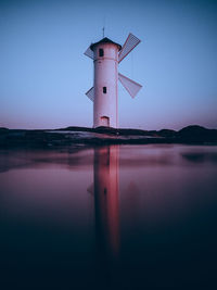 Lighthouse by sea against sky at sunset