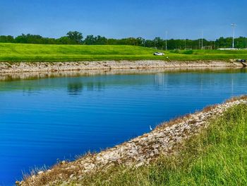 Scenic view of field by lake against blue sky