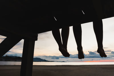 Silhouette feet of couple sitting on the pier at sunset beach