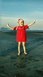 Full length of cheerful girl standing at beach against sky during sunset