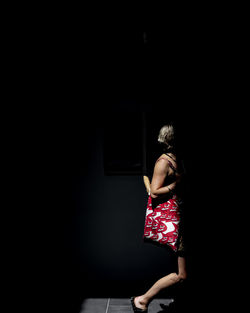 Rear view of woman standing against dark wall
