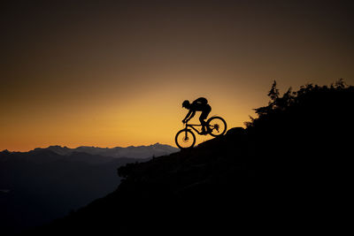 Silhouette man riding bicycle on mountain against sky during sunset