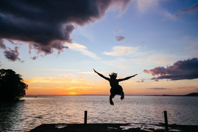 Silhouette man jumping in sea against sky during sunset